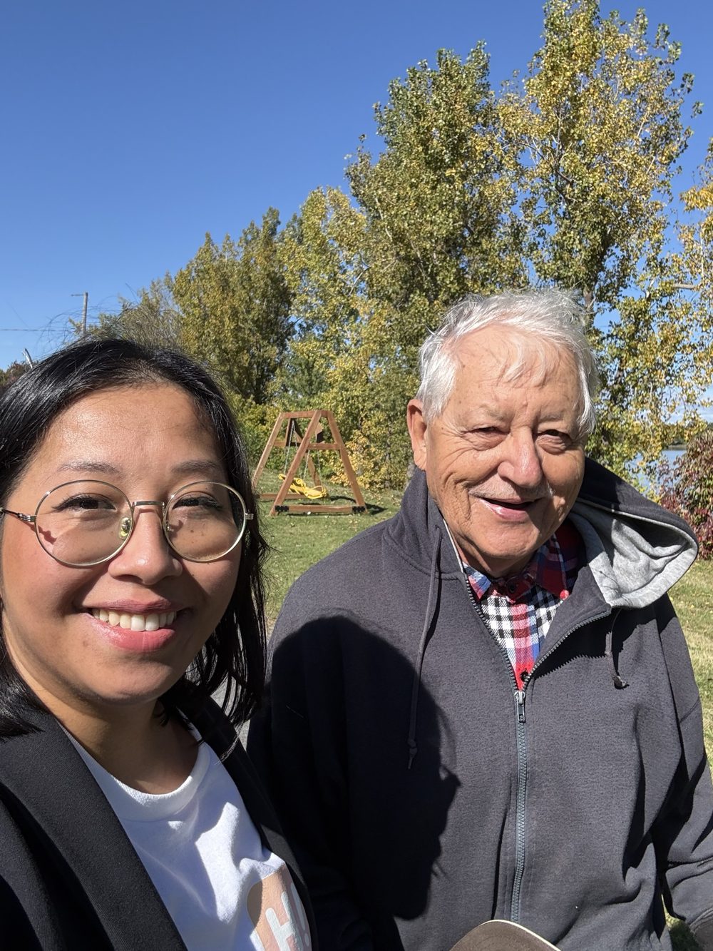 Mary et M. Raymond, souriants, devant une balançoire au bord de l'eau en automne